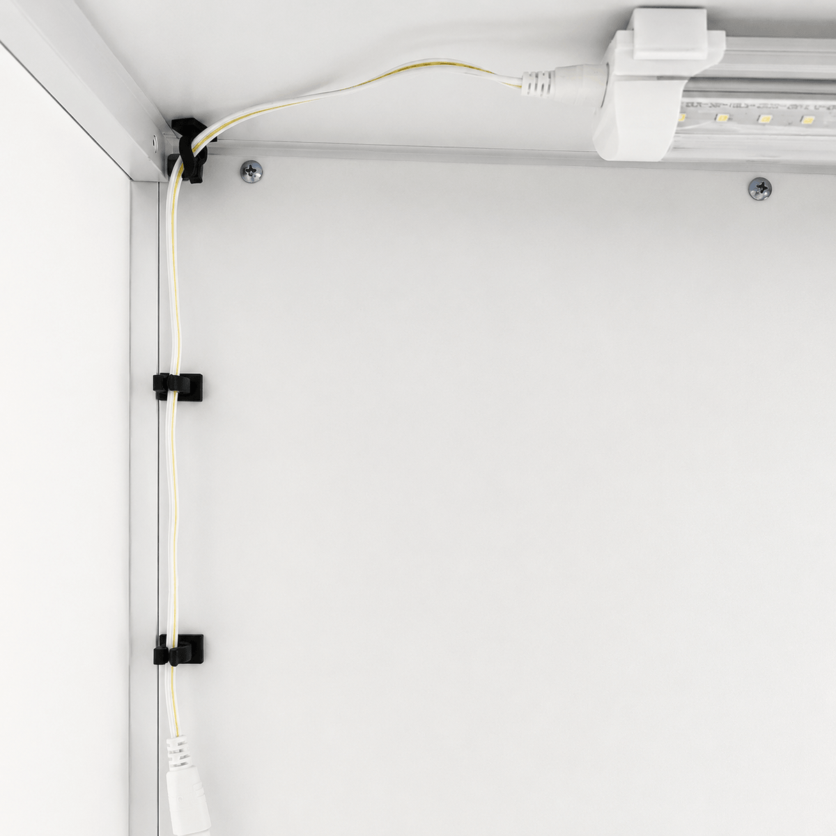 Black cable management clips holding a white power cord along a white metal track, shown in a clean, industrial setting.