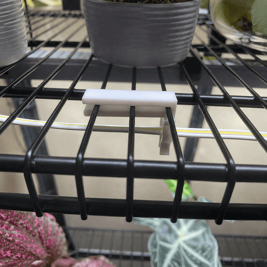 A close-up of a white plastic plant pot caddy clip holding a white pot on a black metal shelving unit.