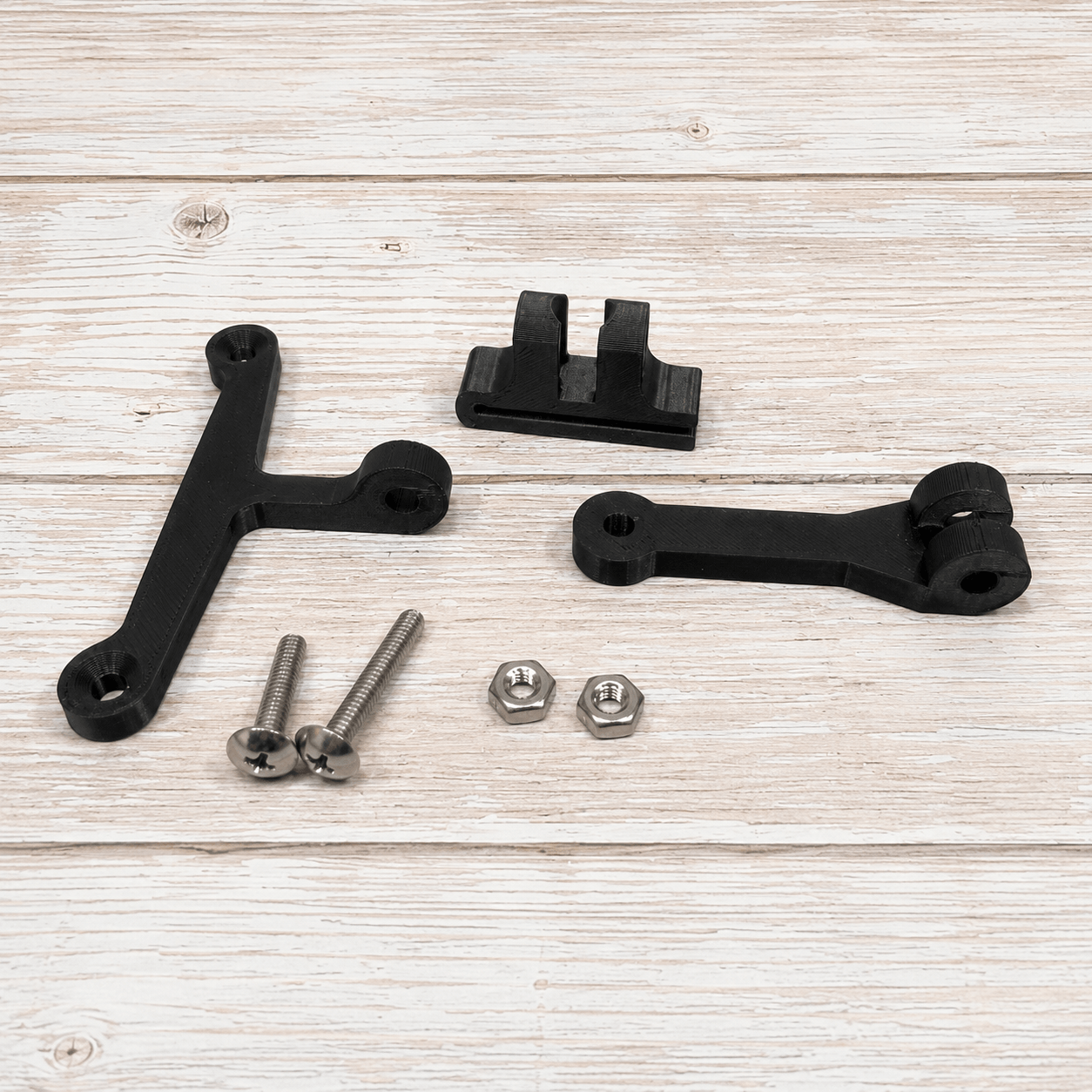 Black metal mounting brackets and silver hardware screws, nuts, and washers arranged on a light wood plank surface.