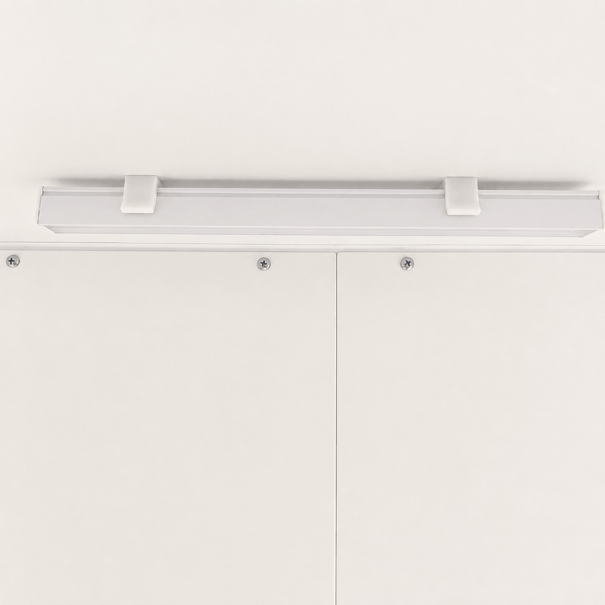 A modern linear LED light fixture with a matte white finish, mounted horizontally on a white ceiling above white cabinet doors.