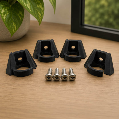 Black corner protectors with screws on a wooden surface, with a plant in the background.