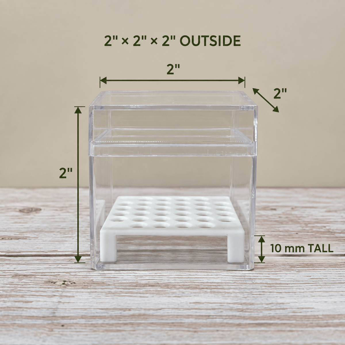 A clear acrylic storage box with a white perforated base, shown on a wooden surface with dimension labels indicating 2 x 2 x 2 inches outside and 10 mm tall.
