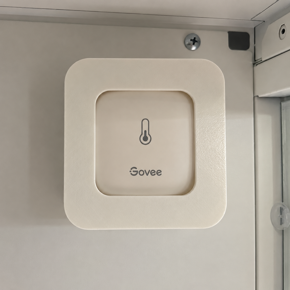 White magnetic mount holding a Govee H5179 hygrometer against the metal interior of a white cabinet.