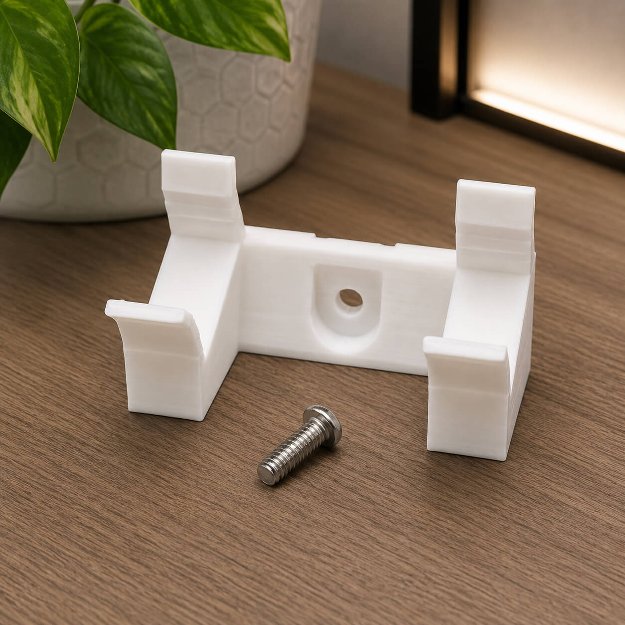 White plastic bracket with a screw on a wooden surface, with a plant in the background.