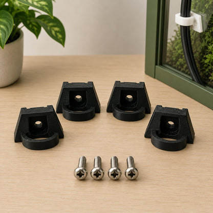 Black plastic brackets and screws on a wooden surface with a plant in the background
