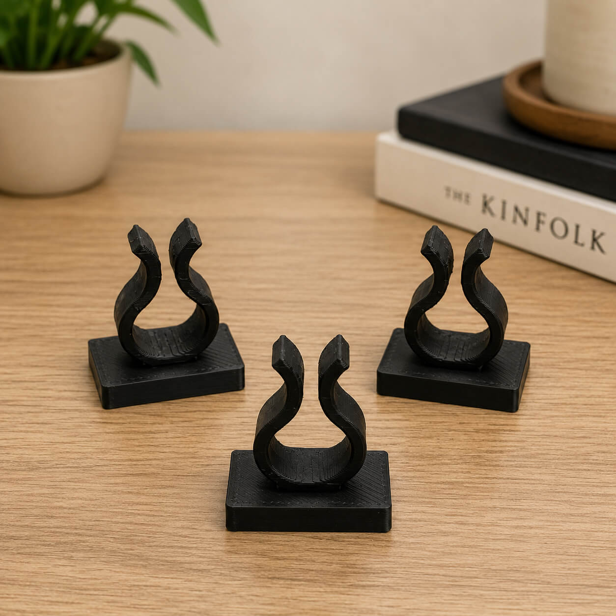 Four black decorative items on a wooden surface with a plant and book in the background.