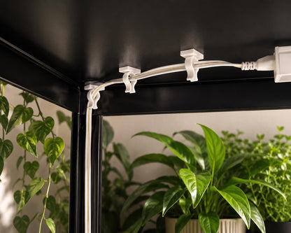 White LED strip light fixture on a black ceiling with plants in the background