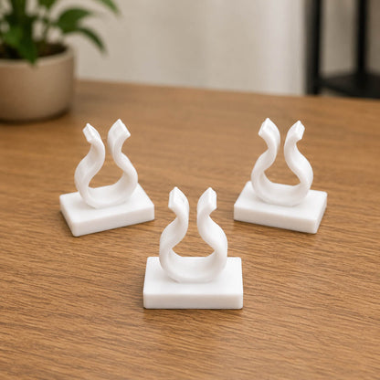 Three white marble swan sculptures on a wooden surface with a blurred plant in the background.