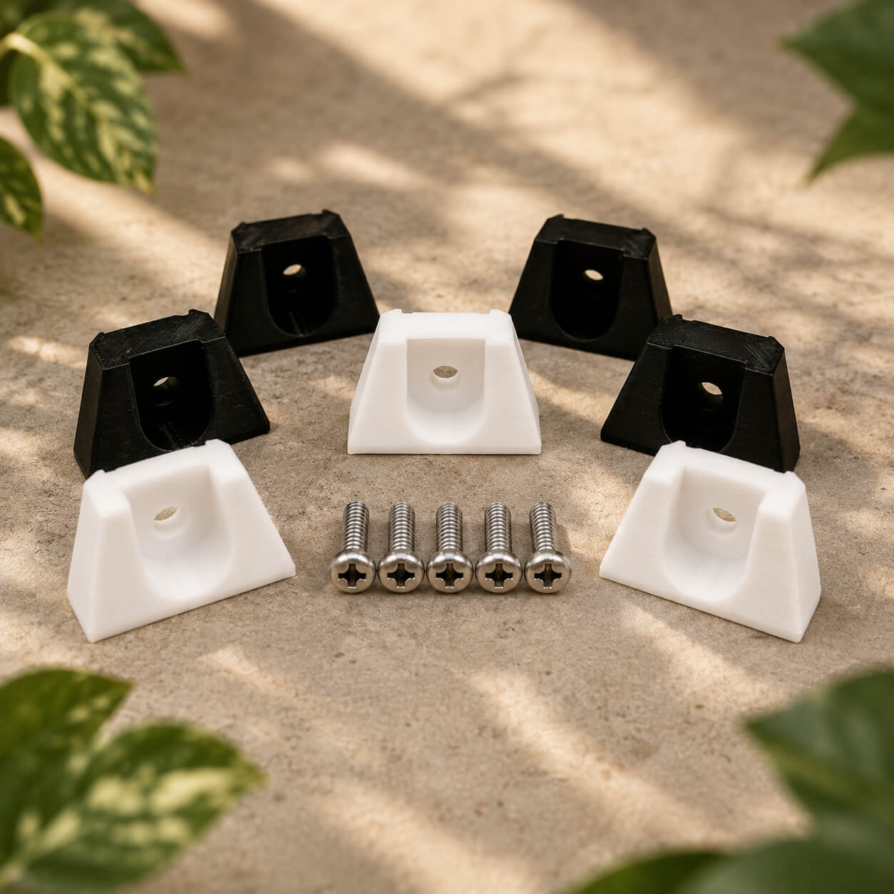 Set of black and white plastic clips with screws on a textured surface with plant leaves in the background