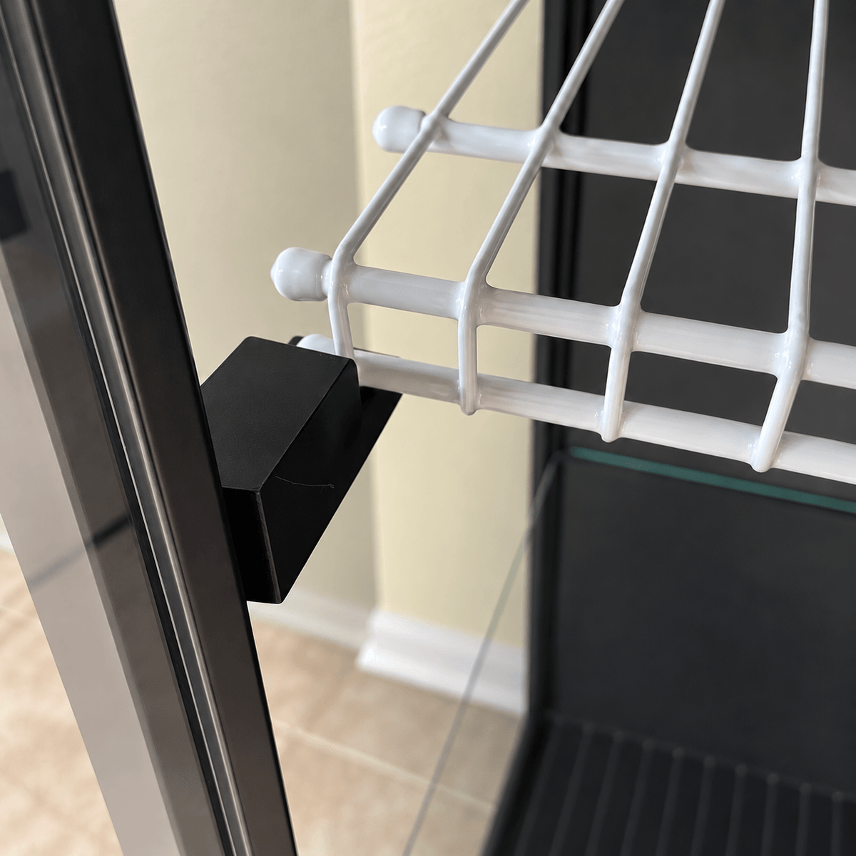 Close-up of a black PETG bracket supporting the white wire shelf at its front edge inside an IKEA Rudsta cabinet.