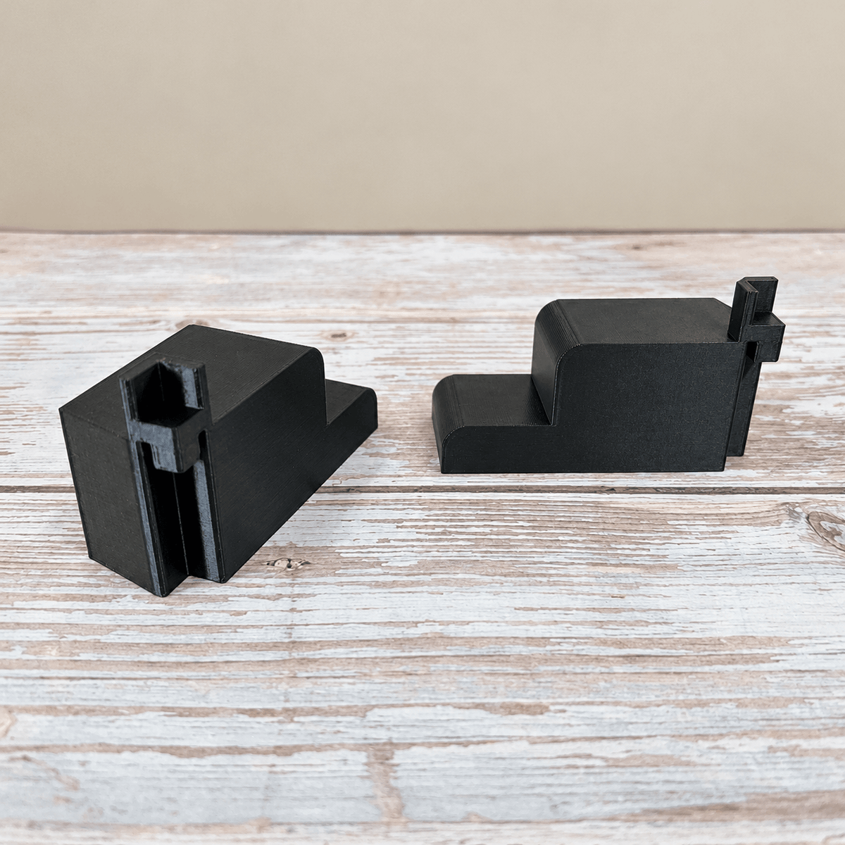 Two black PETG wire shelf brackets for an IKEA Rudsta cabinet, showing the mounting channels and side profile on a whitewashed wood surface.