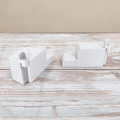 Two white PETG wire shelf brackets for an IKEA Rudsta cabinet, showing the mounting channels and side profile on a whitewashed wood surface.
