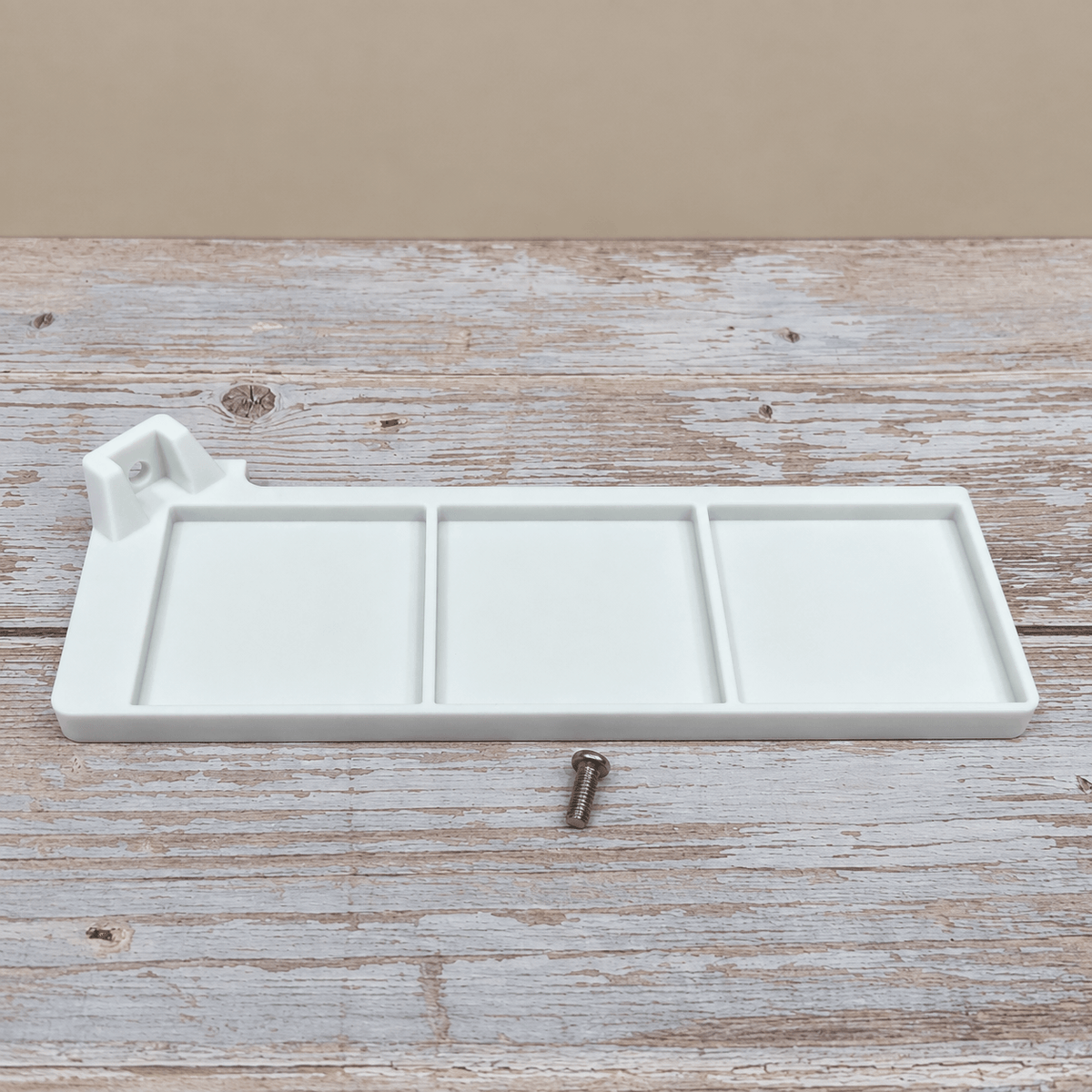 A white three-compartment wall-mounted organizer tray with a small mounting screw, displayed on a rustic whitewashed wooden surface against a beige background.