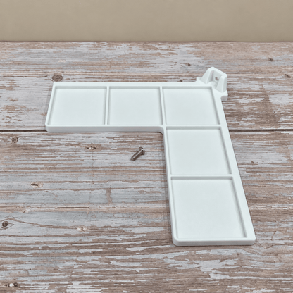 A white plastic L-shaped wall-mounted paint palette with six compartments and a small metal mounting screw, displayed on a rustic wooden surface.