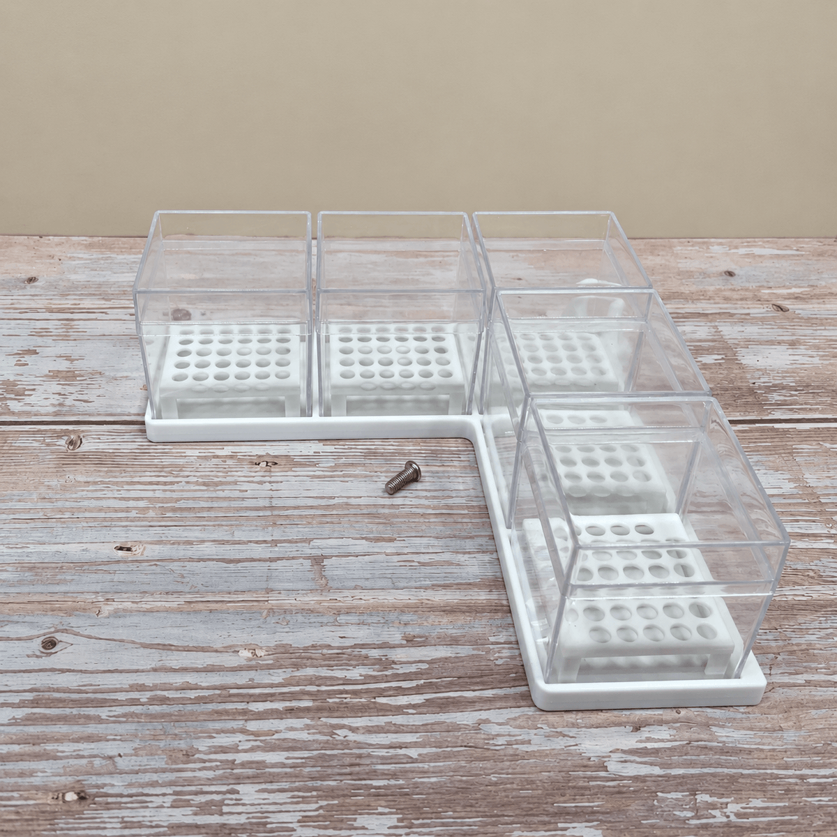 A white plastic L-shaped stand with clear plastic screw-on covers, shown on a rustic wooden tabletop against a beige background.