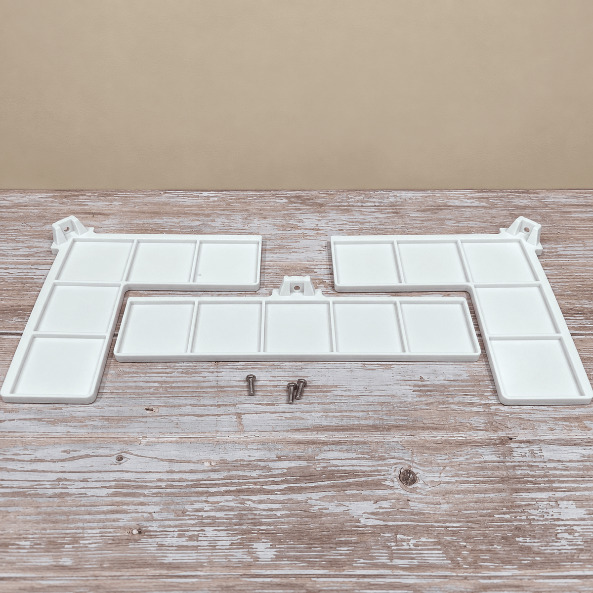 White plastic tray organizer components with multiple rectangular compartments, shown on a rustic wooden surface against a beige background, with two small metal screws below.