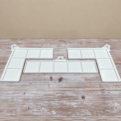 White plastic tray organizer components with multiple rectangular compartments, shown on a rustic wooden surface against a beige background, with two small metal screws below.