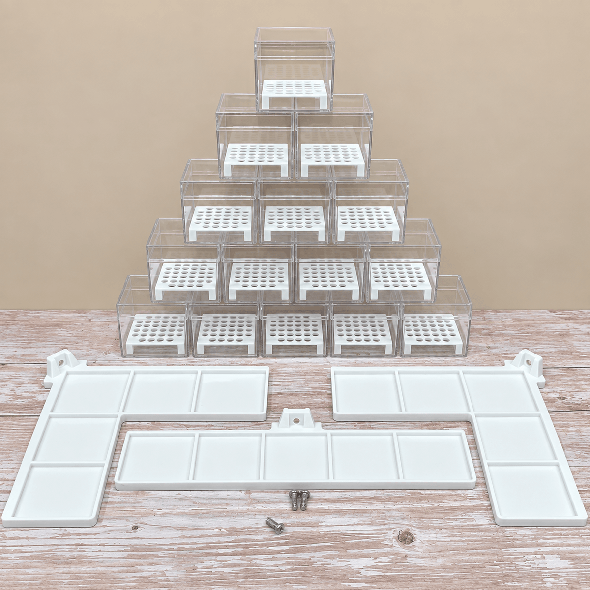 A set of clear plastic organizer drawers with white inserts, arranged in a pyramid stack on a rustic wooden table against a beige background, with white mounting brackets and small screws displayed in front.
