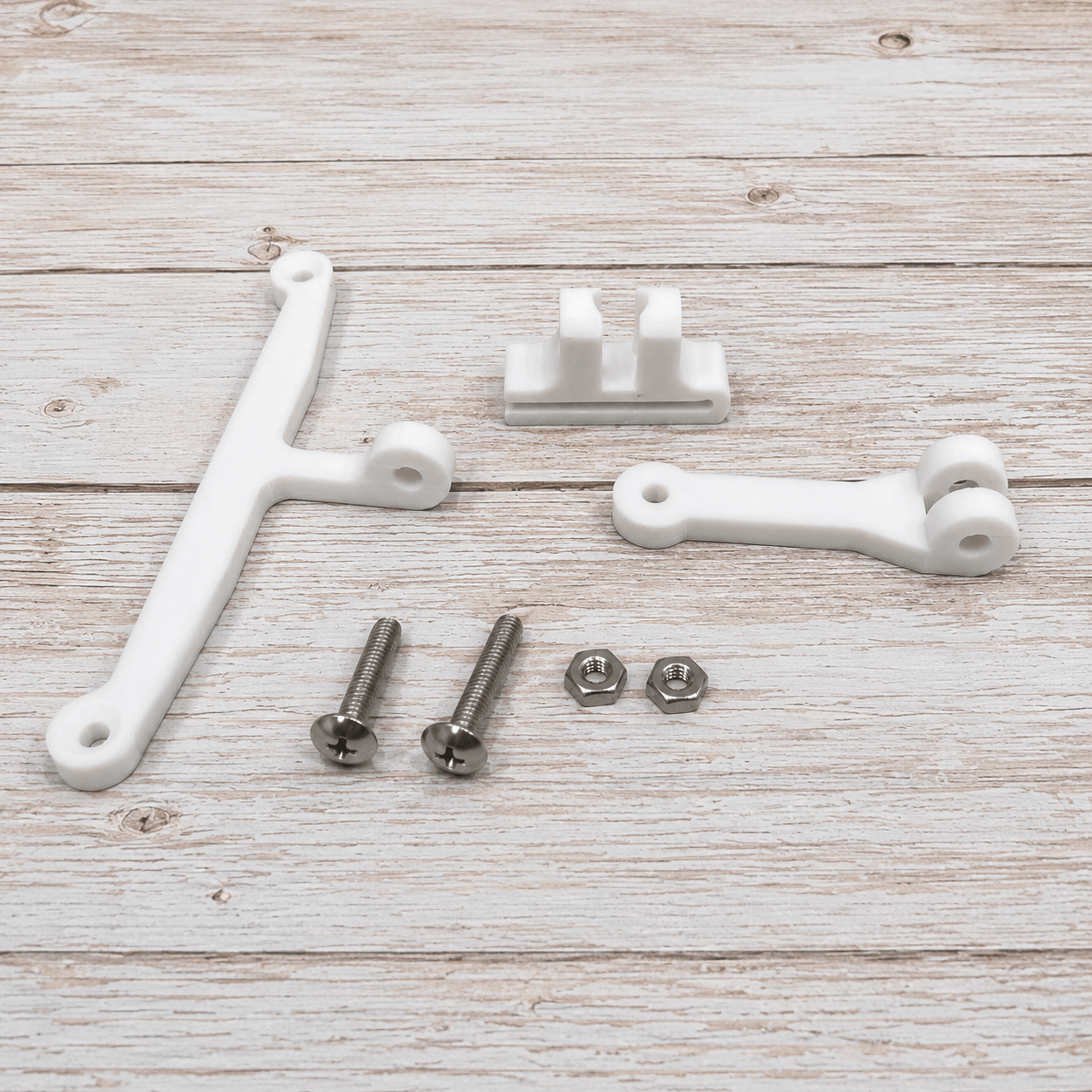 White plastic mounting brackets and silver metal screws and washers laid out on a light wood plank surface.
