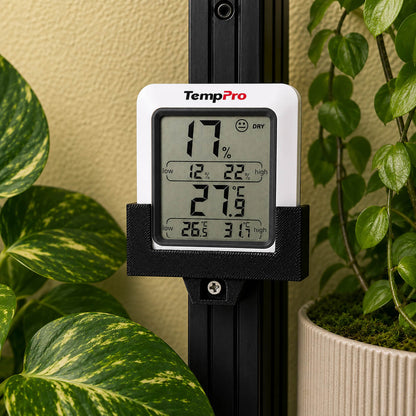 Digital thermometer with humidity and temperature readings in front of green plants