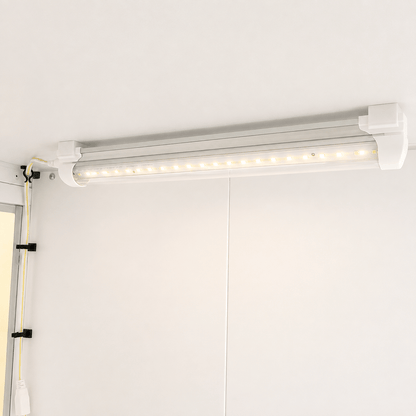 A white LED under-cabinet light bar mounted on a white wall, with its power cord secured on the left using black clips.