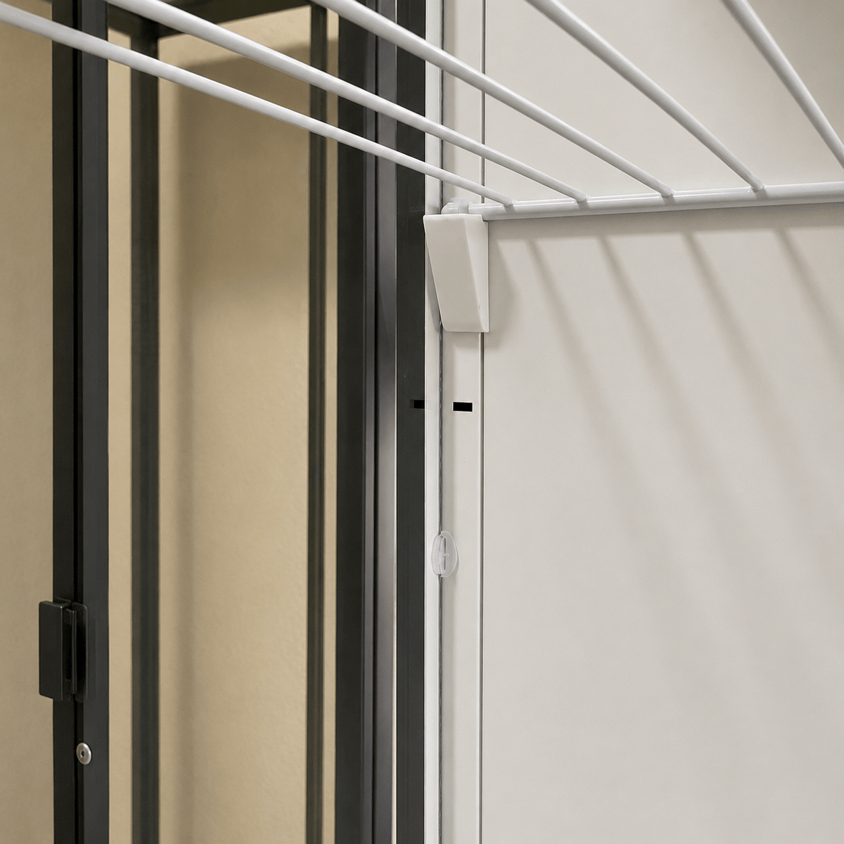 Close-up of a white hanging clothesline mounted on a light-colored wall next to a dark-framed door.
