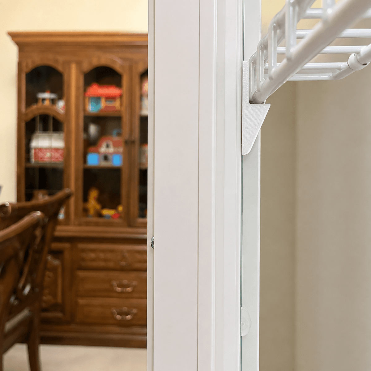 A close-up of a white closet rod frame and hanging rod structure installed in an interior doorway, with a blurred wooden hutch and dining furniture in the background.