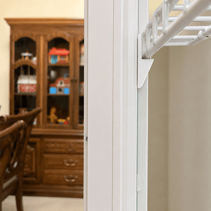 A close-up of a white closet rod frame and hanging rod structure installed in an interior doorway, with a blurred wooden hutch and dining furniture in the background.