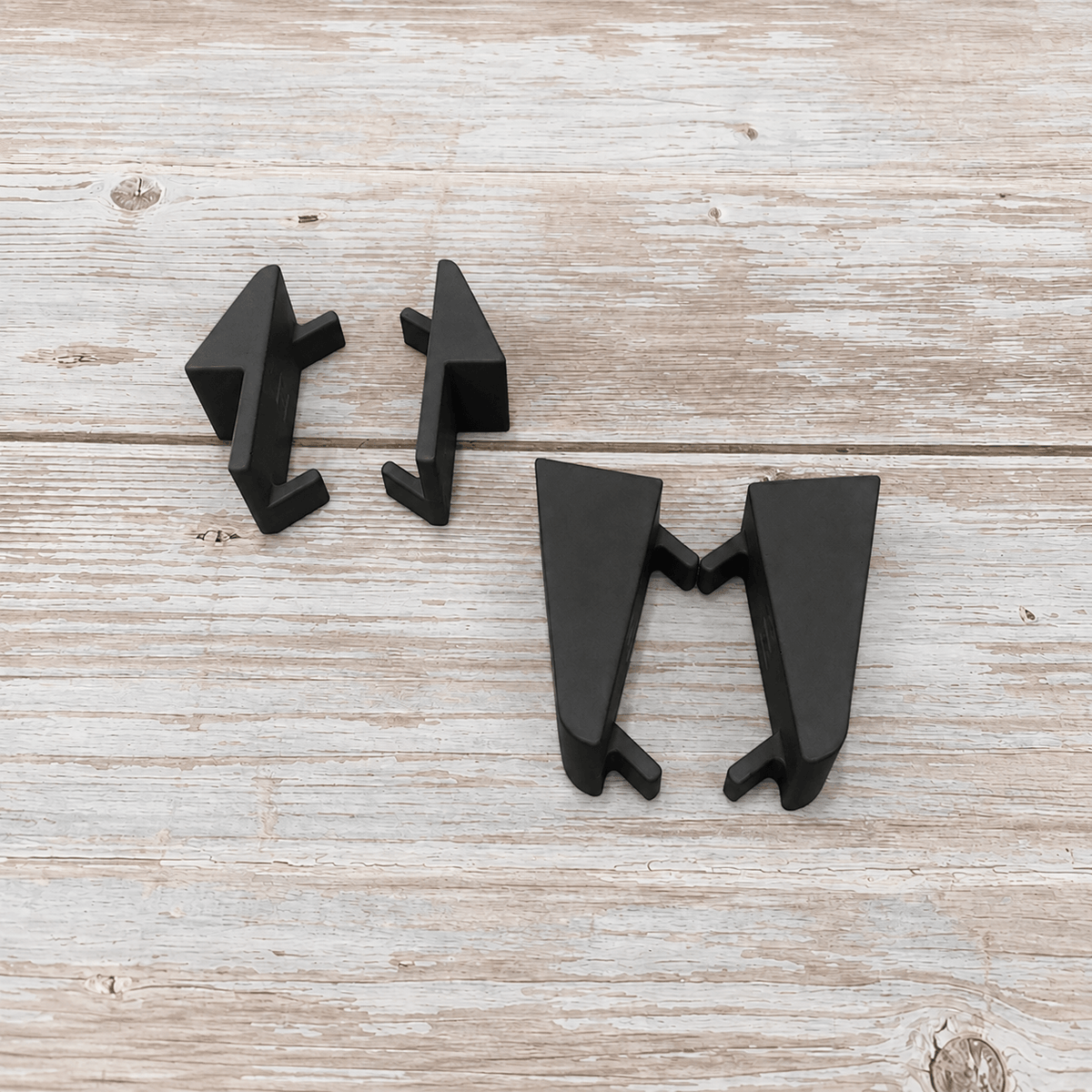 Three matte black geometric drawer pull knobs arranged on a light weathered wood surface.