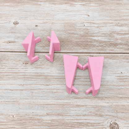 Three pink plastic geometric wall hooks arranged on a light weathered wood surface.
