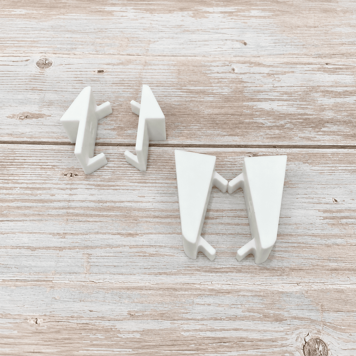 Three white ceramic wall hooks shaped like stylized arrows, arranged on a light rustic wooden surface.