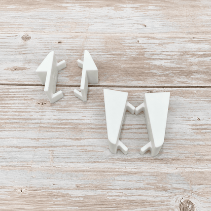 Three white ceramic wall hooks shaped like stylized arrows, arranged on a light rustic wooden surface.