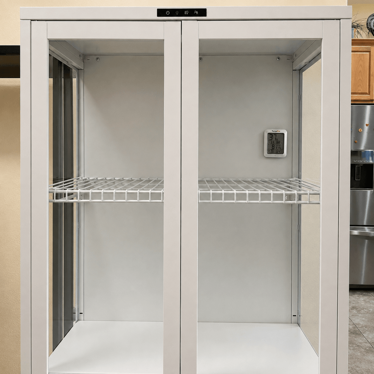 A tall white double-door storage cabinet with wire shelves, shown in a kitchen setting with a stainless steel refrigerator visible on the right.