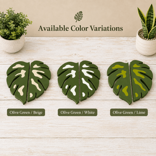 Three pairs of split monstera leaf coasters shown on a light wood surface with the text 'Available Color Variations' above them. The coasters are labeled Olive Green / Beige, Olive Green / White, and Olive Green / Lime, with small potted plants at the top corners.