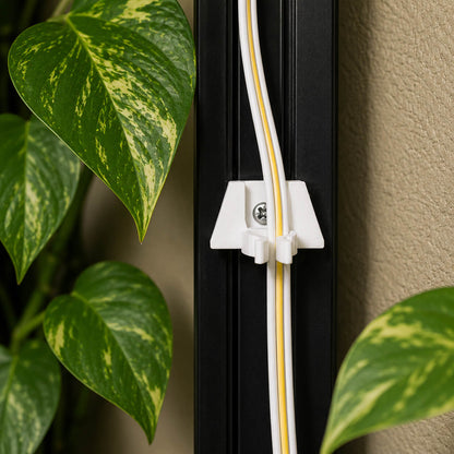 White and gold cable management clip on a black surface with green leaves in the background