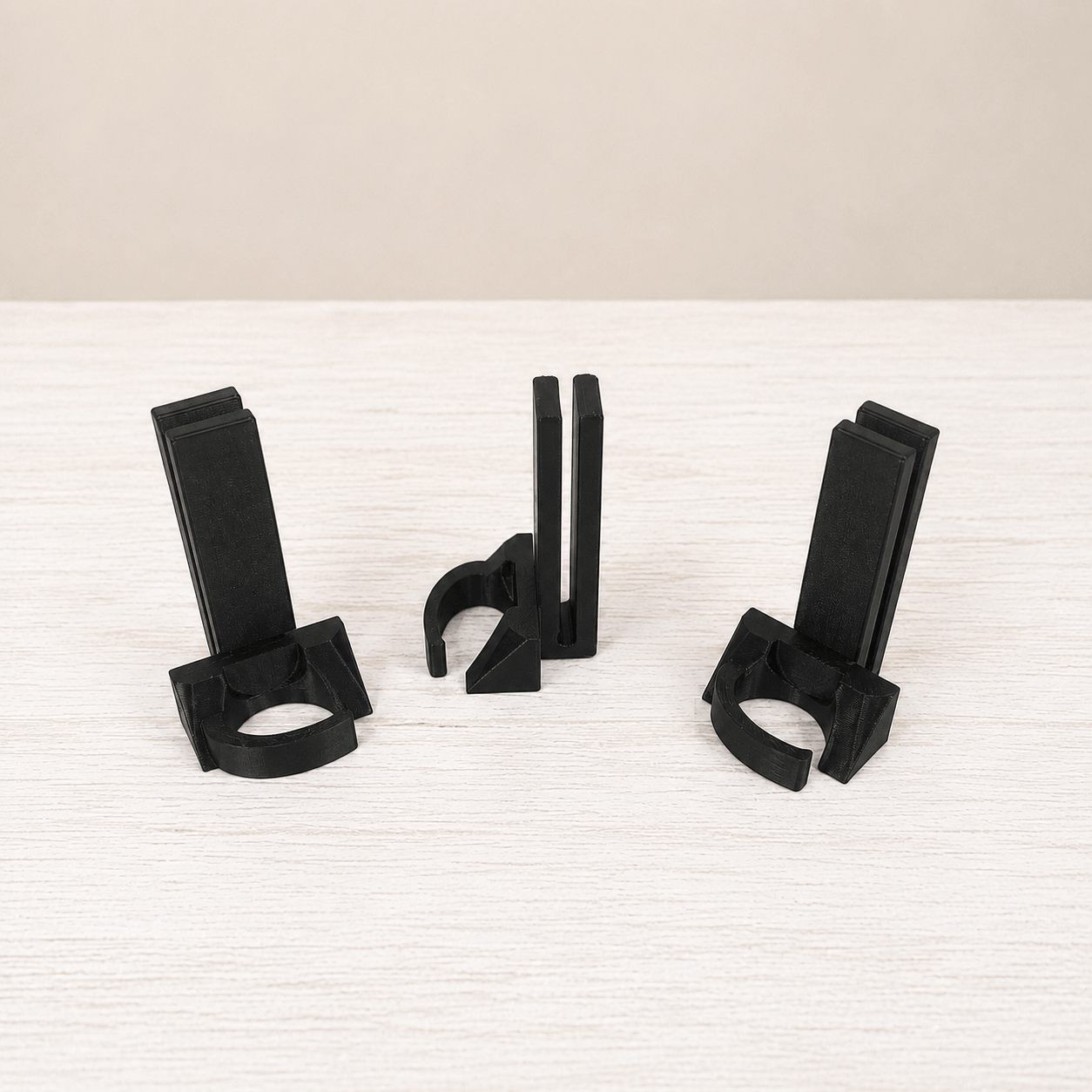 Three black plastic cable management clips arranged on a light-colored wooden surface against a neutral beige background.