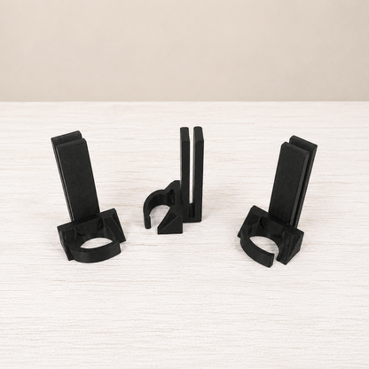 Three black plastic cable management clips arranged on a light-colored wooden surface against a neutral beige background.