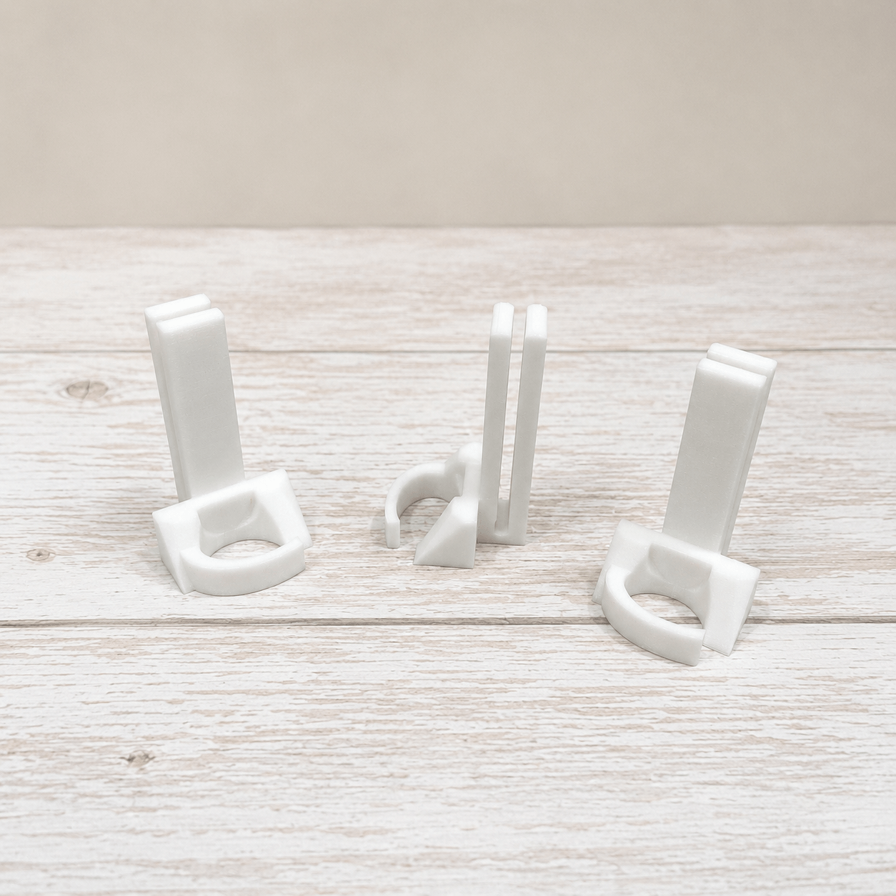 Three small white plastic hook-like accessories arranged on a light whitewashed wooden surface against a pale beige background.