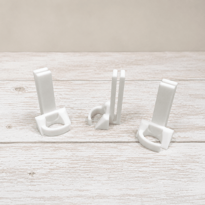Three small white plastic hook-like accessories arranged on a light whitewashed wooden surface against a pale beige background.