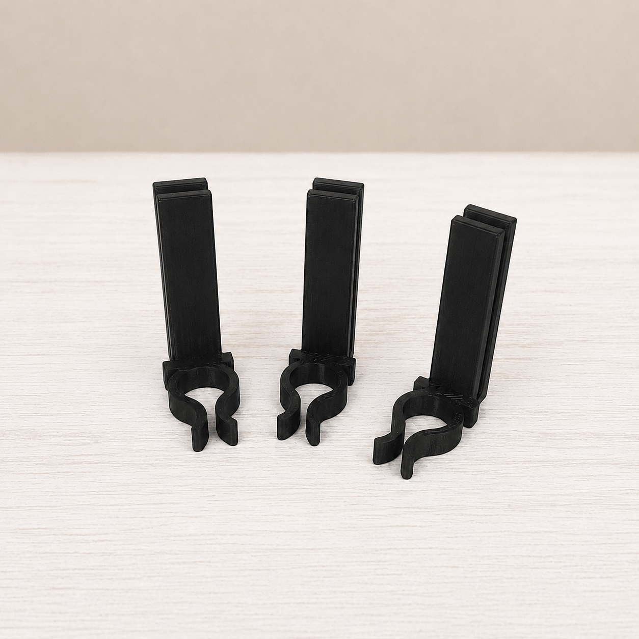 Three black plastic clip-on stands arranged upright on a light wood surface against a beige background.