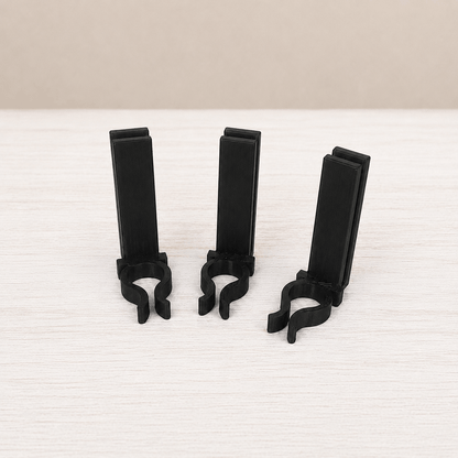 Three black plastic clip-on stands arranged upright on a light wood surface against a beige background.