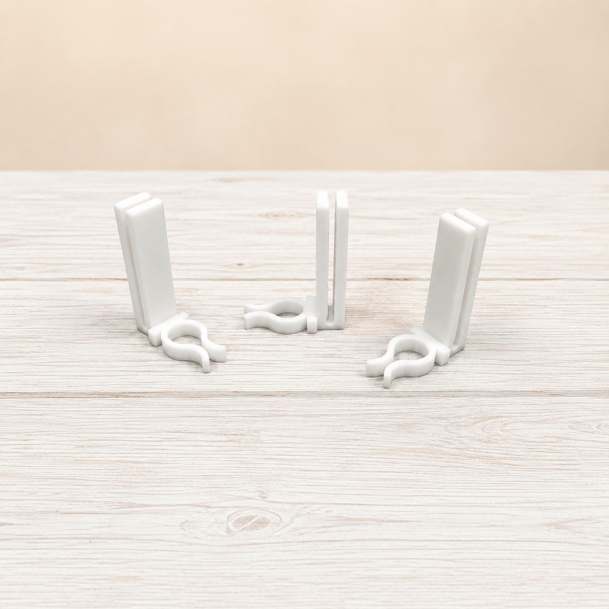 Three white plastic bookends arranged on a light wood-grained surface against a beige background.