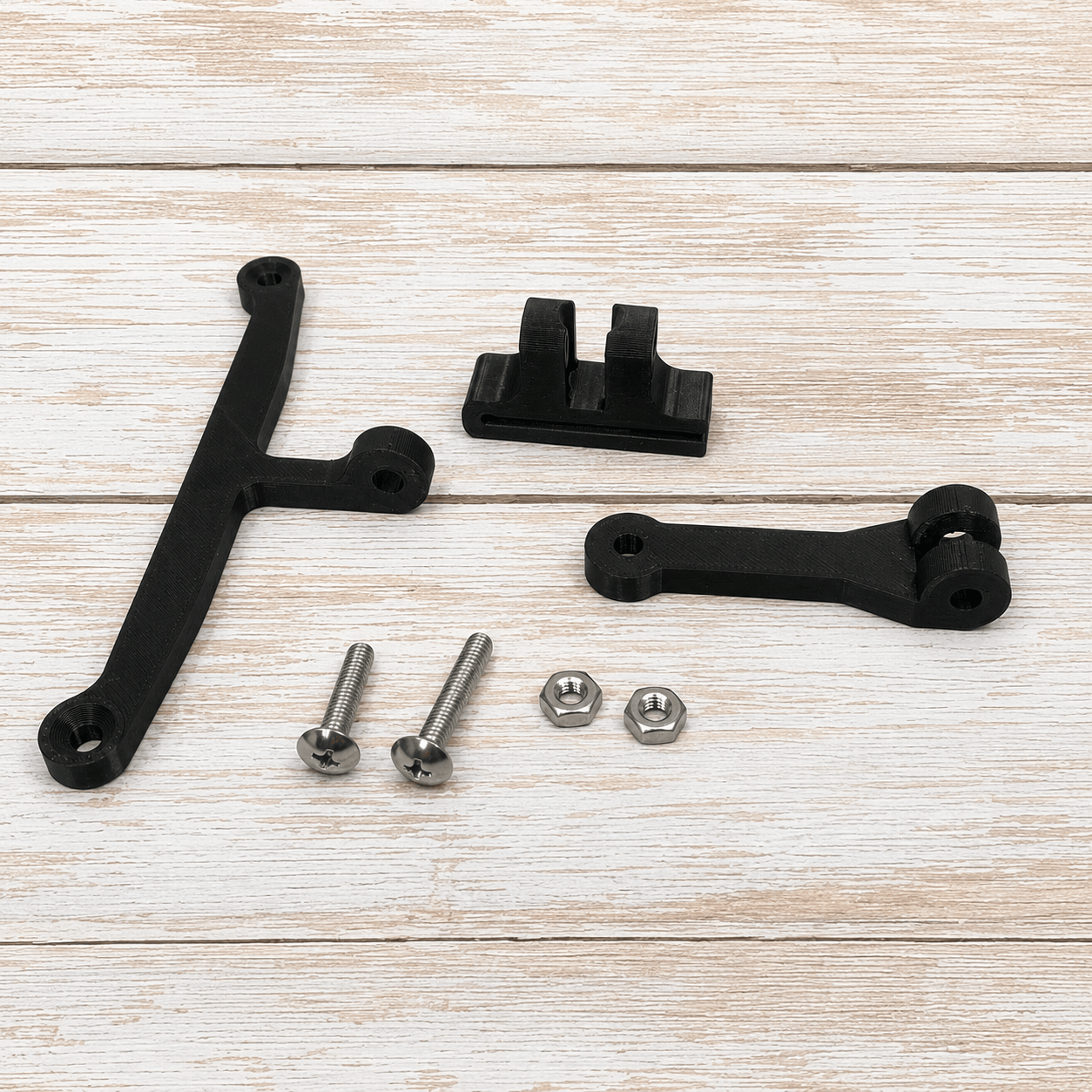Black metal mounting hardware set including two black brackets, two silver screws, and two silver nuts, arranged on a light wood plank background.