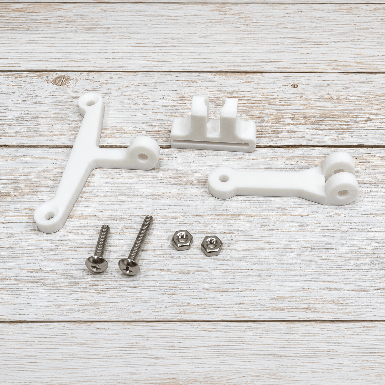 Three white plastic mounting brackets with silver screws, nuts, and washers, arranged on a light whitewashed wooden background.